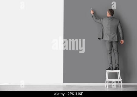 Mature business consultant with marker on stepladder near black and white wall, back view Stock Photo