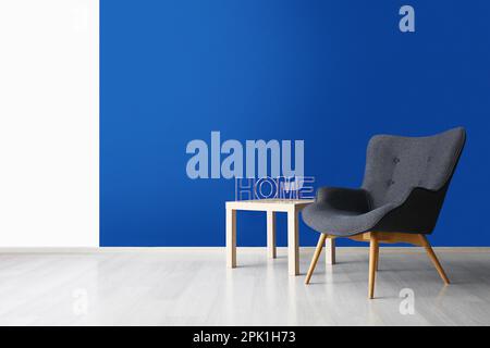 Stylish grey armchair and word HOME on table near blue wall Stock Photo