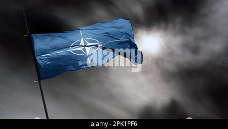 Flag of NATO waving in the wind on flagpole against the sky Stock Photo