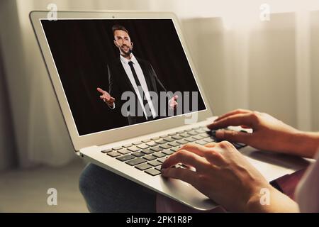Woman watching performance of motivational speaker on laptop indoors, closeup Stock Photo