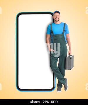 Repair service - just call. Happy professional repairman holding toolbox and smartphone with blank screen on beige background, space for design Stock Photo