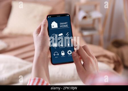 Woman using Smart Home app on mobile phone indoors, closeup Stock Photo