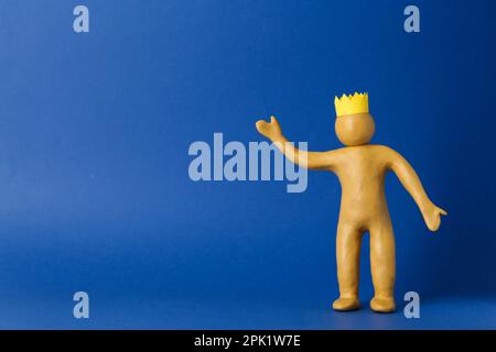 Plasticine figure with crown on head against blue background. Space for text Stock Photo