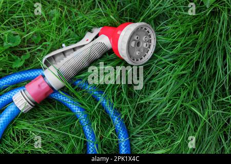 Watering hose with sprinkler on green grass outdoors, top view Stock Photo
