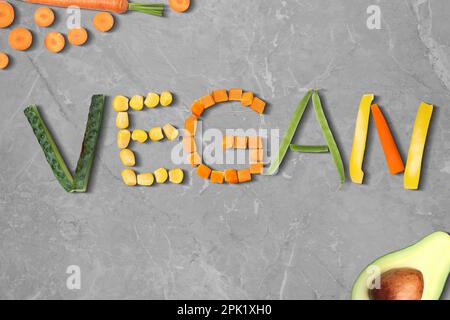Word VEGAN made of different fresh tasty vegetables on light grey marble background, flat lay Stock Photo