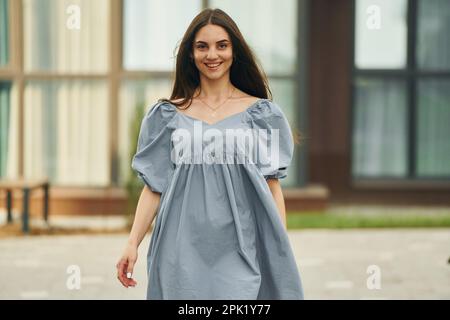 Beautiful young woman walking in dress in the city. Building exterior Stock Photo