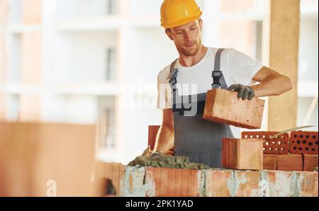 Building process. Young man working in uniform at construction at daytime. Stock Photo
