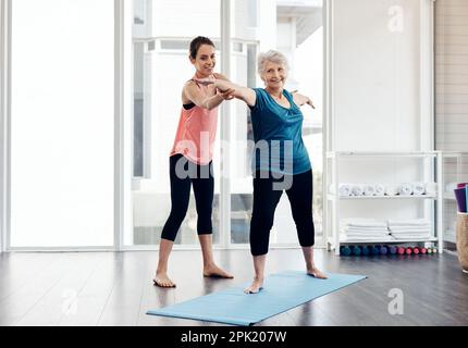Seniors with active lifestyles experience a wealth of health advantages. a fitness instructor helping a senior woman during a yoga class. Stock Photo