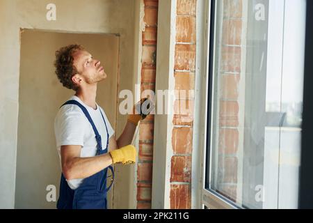 In protective gloves. Young man working in uniform at construction at daytime Stock Photo