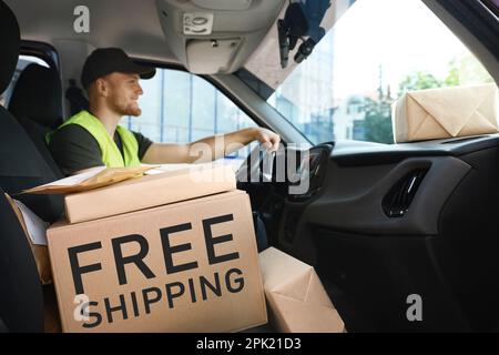 Young courier with parcels in delivery car. Free shipping Stock Photo
