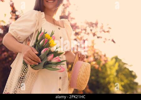 Young woman with bouquet of tulips and hat in park on sunny day, closeup. Space for text Stock Photo