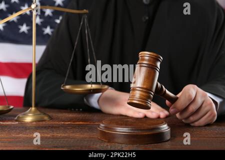 Judge with gavel at wooden table near flag of United States, closeup Stock Photo