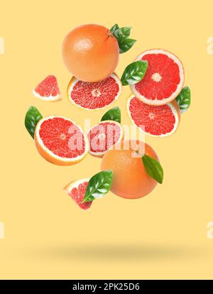 Tasty ripe grapefruits and green leaves falling on beige background Stock Photo