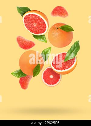 Tasty ripe grapefruits and green leaves falling on beige background Stock Photo