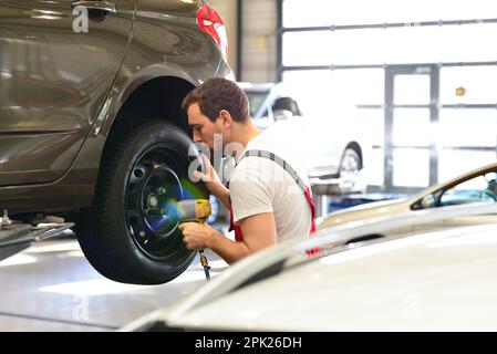 professional car mechanic works in a workshop and changes tyres on the vehicle Stock Photo