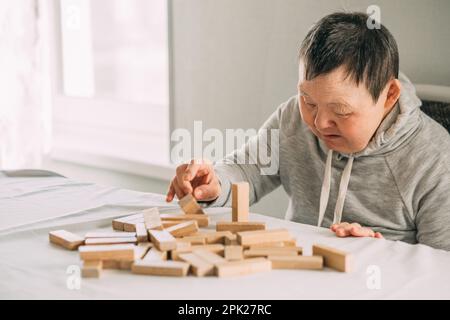 elderly woman with down syndrome and an Asian girl play in tower from wooden blocks Stock Photo