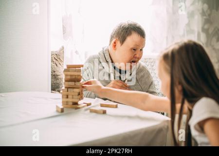 elderly woman with down syndrome and an Asian girl play in tower from wooden blocks Stock Photo