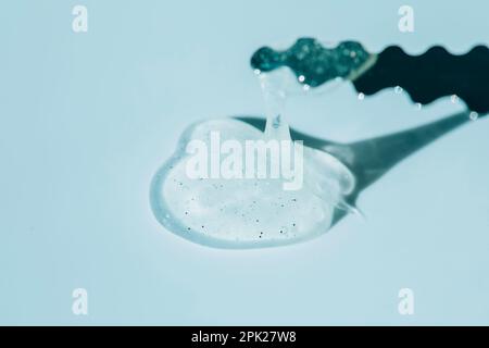 The texture of a liquid gel cosmetic product with a metal tool on a transparent blue background Stock Photo