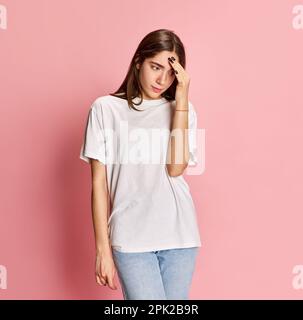 Portrait of young girl in casual clothes holding hand to head with thoughtful expression against pink studio background. Forget about something Stock Photo