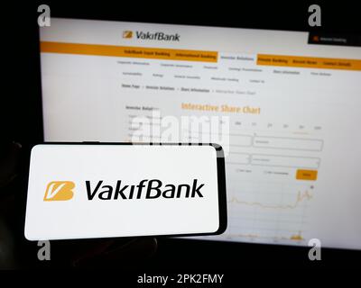 Person holding mobile phone with logo of Turkiye Vakiflar Bankasi T.A.O. (VakifBank) on screen in front of web page. Focus on phone display. Stock Photo