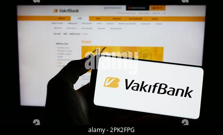 Person holding cellphone with logo of Turkiye Vakiflar Bankasi TAO (VakifBank) on screen in front of business web page. Focus on phone display. Stock Photo