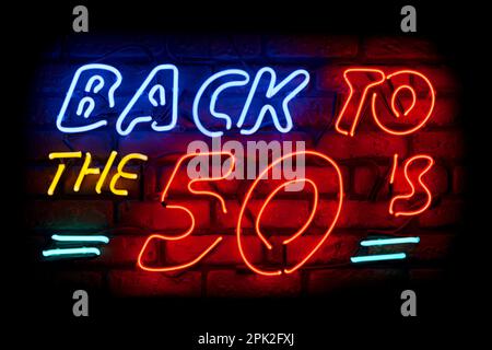 Neon light on a brick wall saying; Back to the 50's. Stock Photo