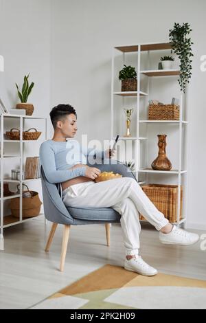 Vertical full length portrait of pregnant woman with tattoos using smartphone in minimal design interior Stock Photo