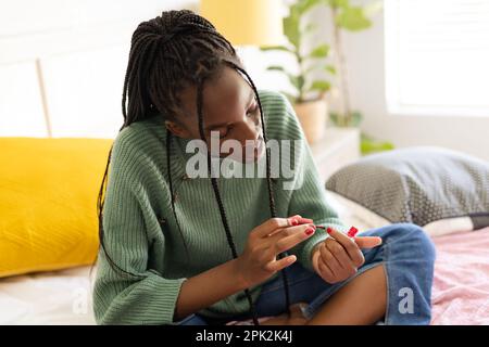 African american teenager girl sitting on bed and painting nails Stock Photo