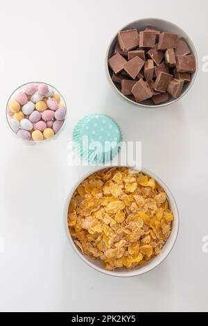 Ingredients in bowls for making chocolate nests - cornflakes, chocolate chunks, mini eggs and cupcake cases (Easter) Stock Photo