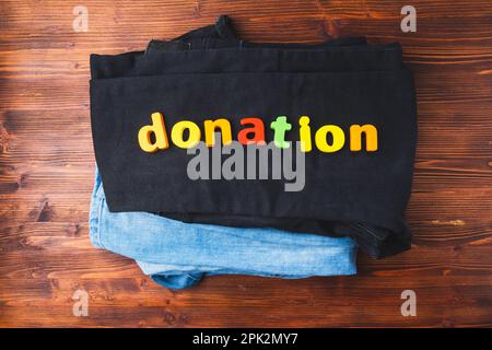 Clothes and an inscription: the donation is on it. Symbol of charity, wooden background Stock Photo