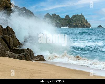 Sea, surf, waves and spray with Logan rock headland in the distance, Porthcurno beach, Cornwall, England, UK Stock Photo