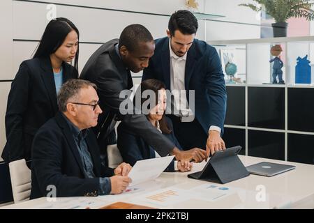 Group of diverse colleagues in formal clothes standing and sitti Stock Photo