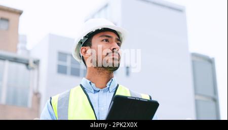 Construction worker holding a digital tablet while doing inspection. Organized male engineer or technician in a hardhat checking project plan with Stock Photo
