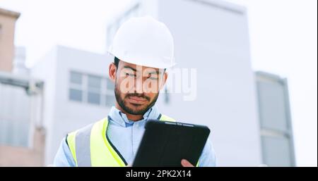 Construction worker holding a digital tablet while doing inspection. Organized male engineer or technician in a hardhat checking project plan with Stock Photo