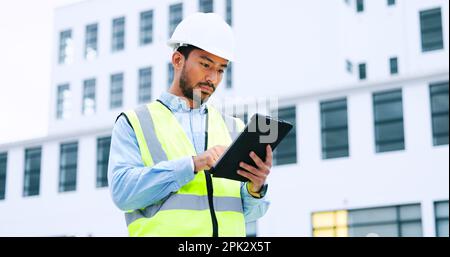 Male engineer checking data on digital tablet and inspecting construction site. Technician in a hardhat doing management and project planning outdoors Stock Photo
