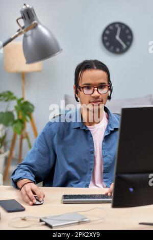 Vertical portrait of young black man using computer at home while studying or writing code Stock Photo