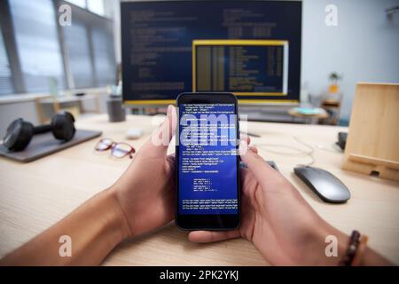 POV of male hands holding smartphone with code lines while programming mobile app, copy space Stock Photo