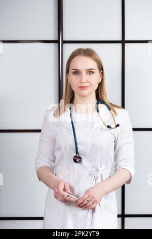 Portrait of a young woman doctor in a white uniform with a stethoscope around her neck. Family doctor, cardiologist or nurse Stock Photo