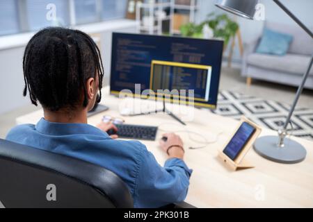 Back view at black young man writing code while studying computer programming at home, copy space Stock Photo