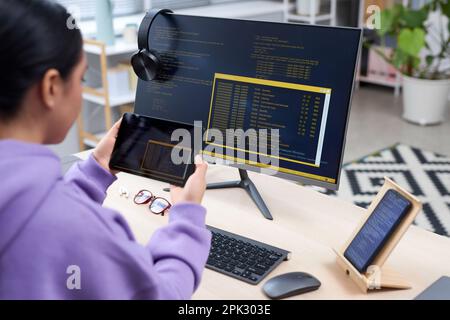 Side view of female IT programmer holding tablet and writing code for mobile devices at workplace Stock Photo