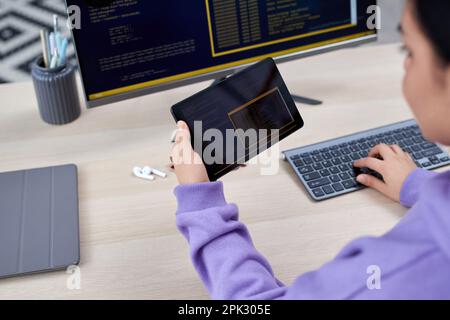 Close up of female computer programmer holding digital tablet and writing code for mobile devices at desk Stock Photo
