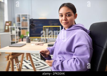 Portrait of young woman as IT programmer looking at camera at workplace with code screens in background, copy space Stock Photo