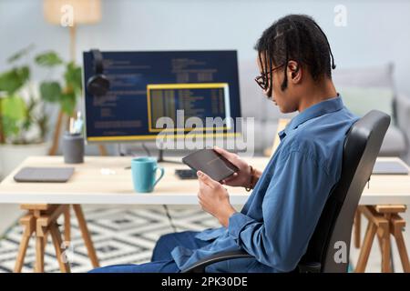 Side view of male IT programmer holding tablet and writing code for mobile devices at workplace Stock Photo