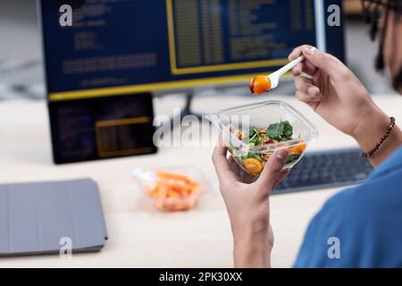 Closeup of unrecognizable man eating takeout lunch at workplace while writing code Stock Photo