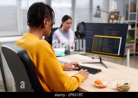 Back view of young black man writing code while working at desk in office, copy space Stock Photo