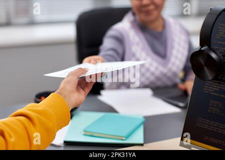 Close up of two young people handing document across table in office while collaboration on IT project, copy space Stock Photo