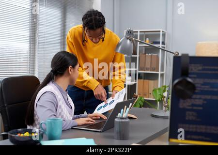 Portrait of two young people discussing document while collaborating on project in IT development office Stock Photo