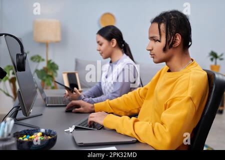 Side view portrait of two young people writing code in office with focus on black man in foreground Stock Photo