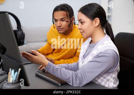 Two young people writing code in office with focus on multiethnic woman pointing at computer screen Stock Photo