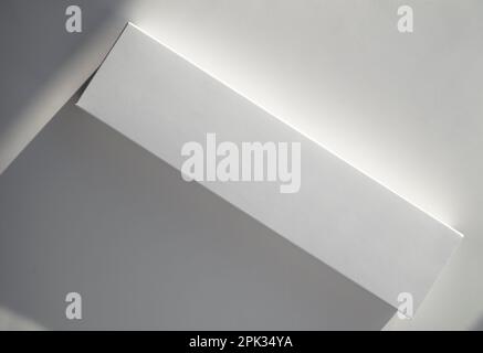 Real rectangle paper box with sunlight on surface. Blank cardboard package and shadows on a office desk. Minimal composition. Stock Photo